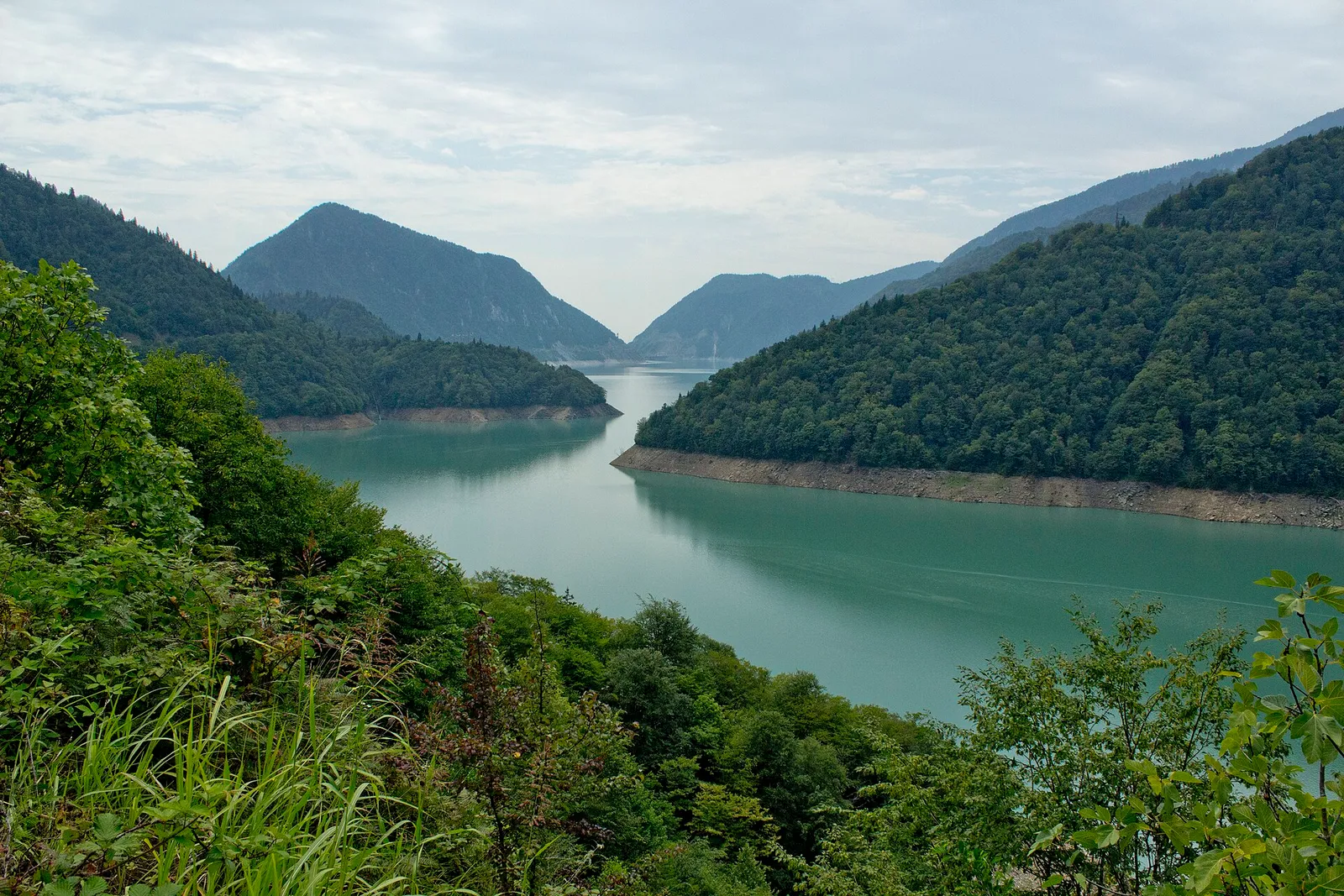 The turquoise water of the Enguri reservoir below forested slopes in Georgia