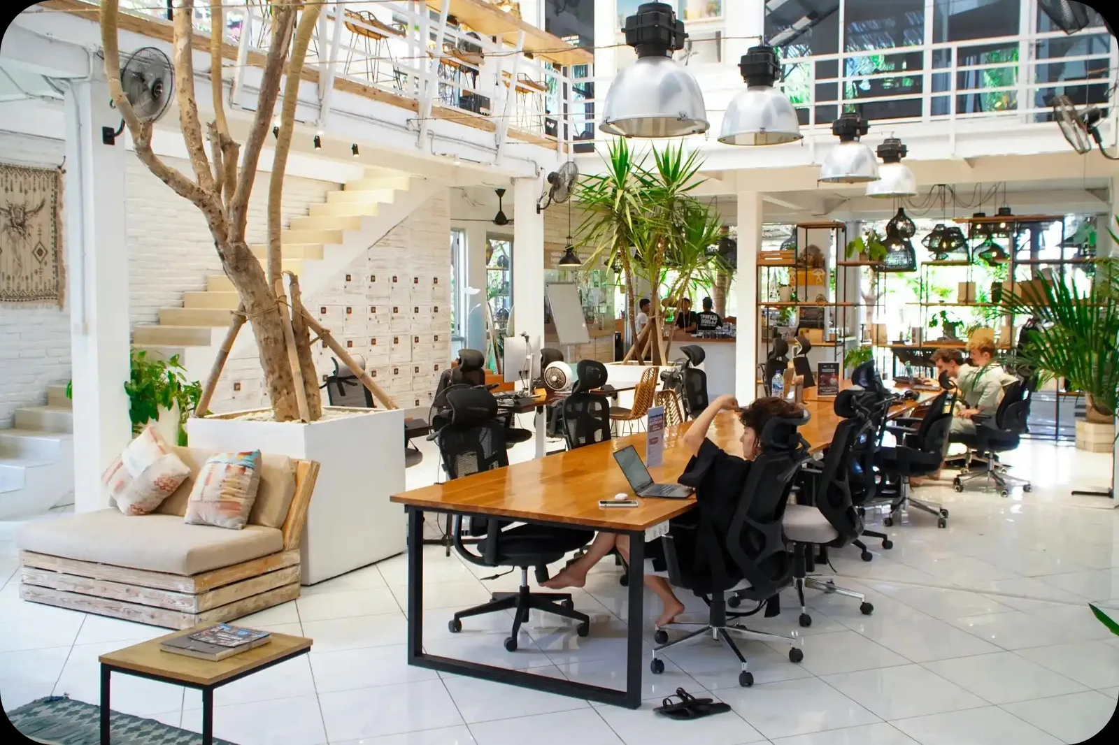 נוודים דיגיטליים עובדים במרחב העבודה המשותף של פבריקה בטביליסי גאורגיה מול חלונות תעשייתיים גדולים