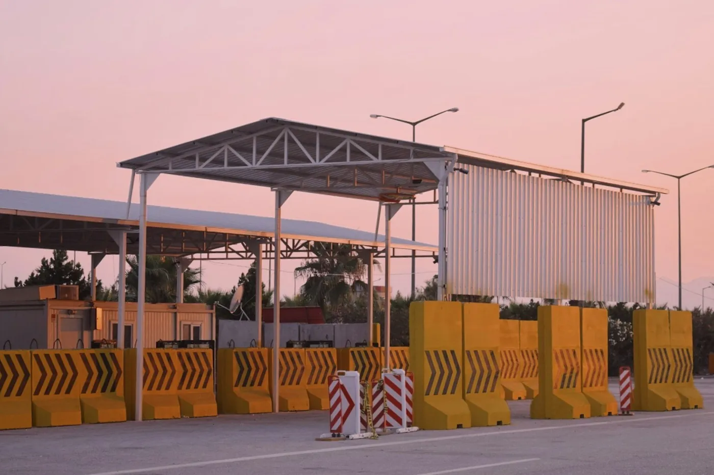 A road border checkpoint with a steel canopy and concrete barriers at dusk