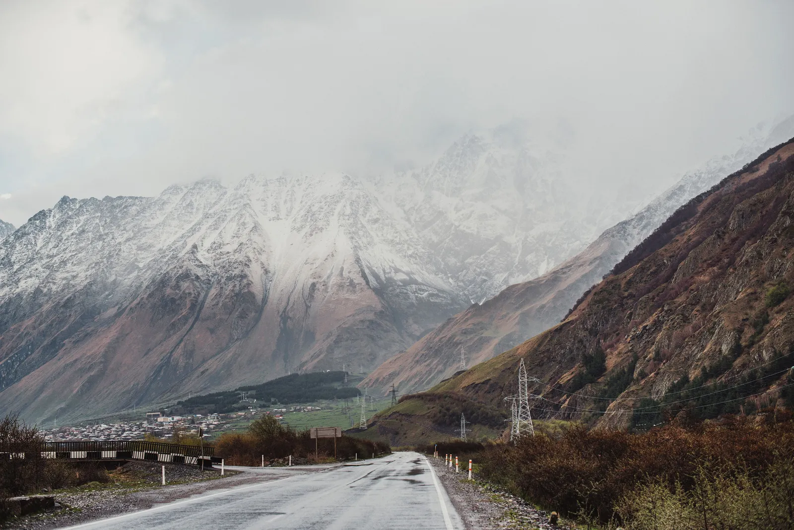 The Georgian Military Highway running towards snow covered peaks above a village in the Kazbegi valley, Georgia