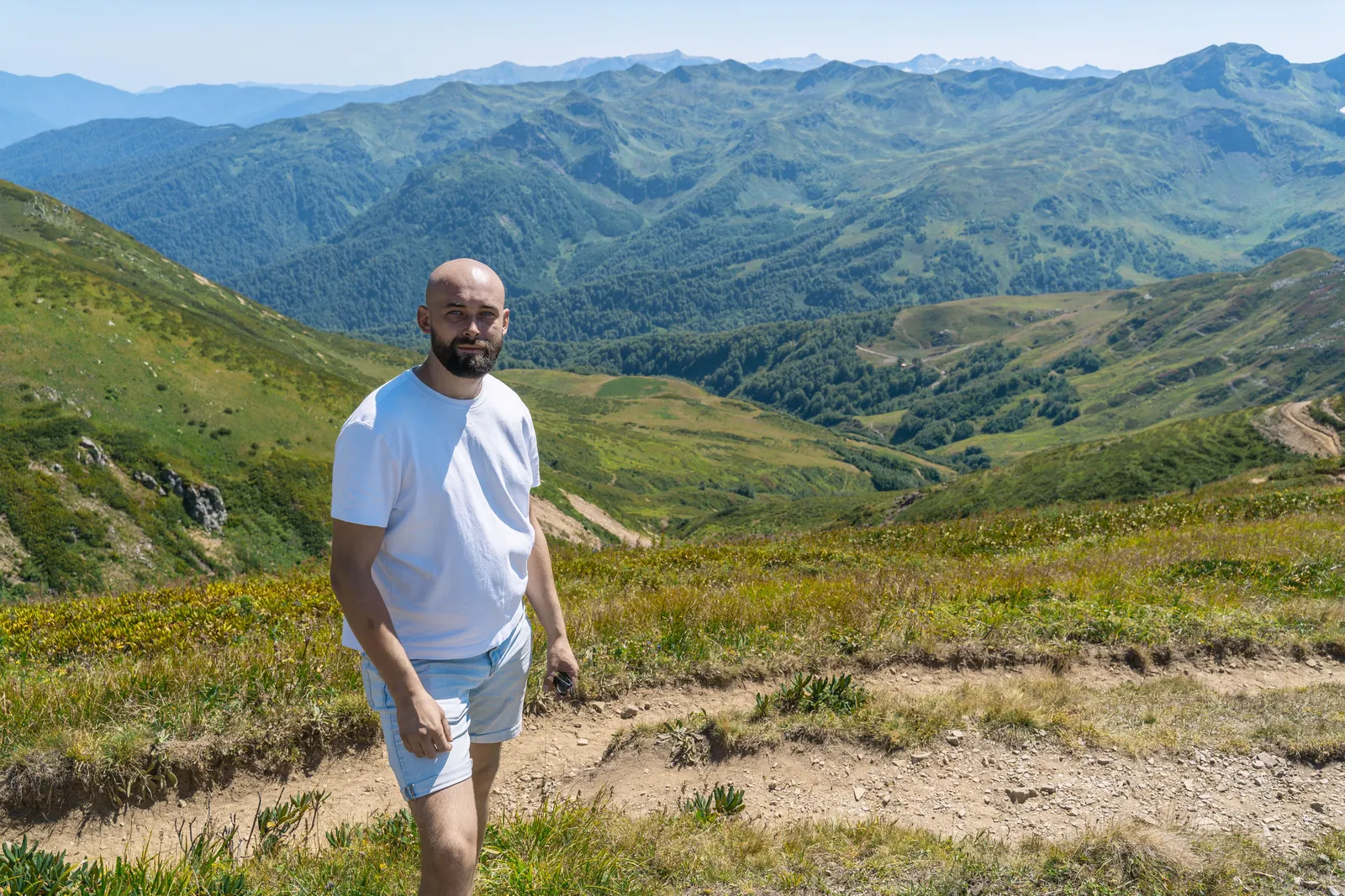 A lone walker on a mountain trail above a green valley in the Georgian Caucasus