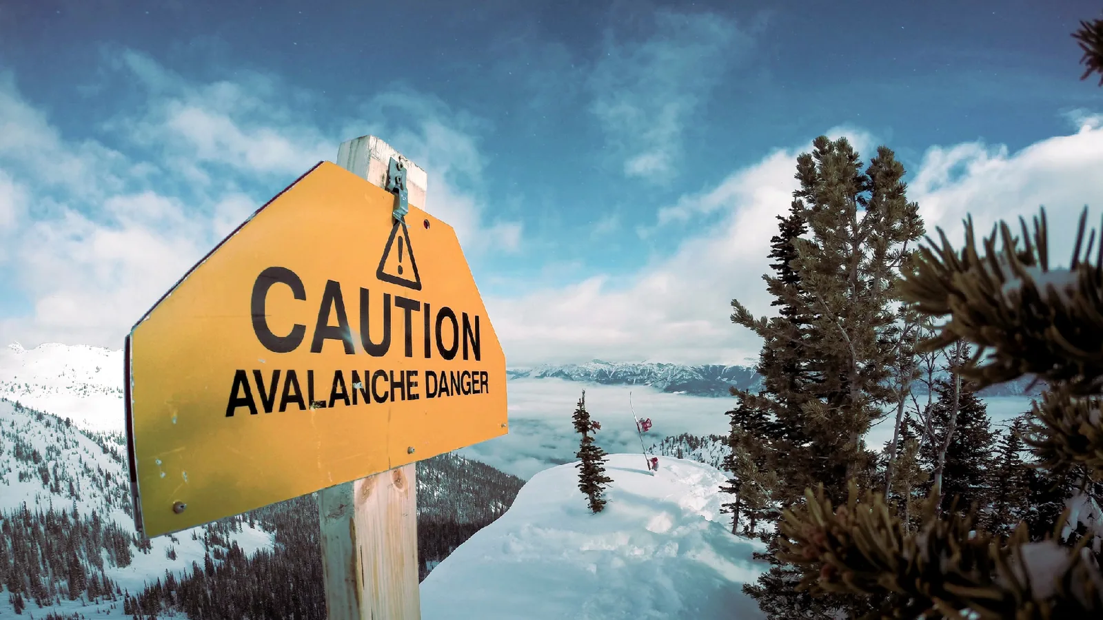 A yellow avalanche danger warning sign in the snow at a Georgian ski area