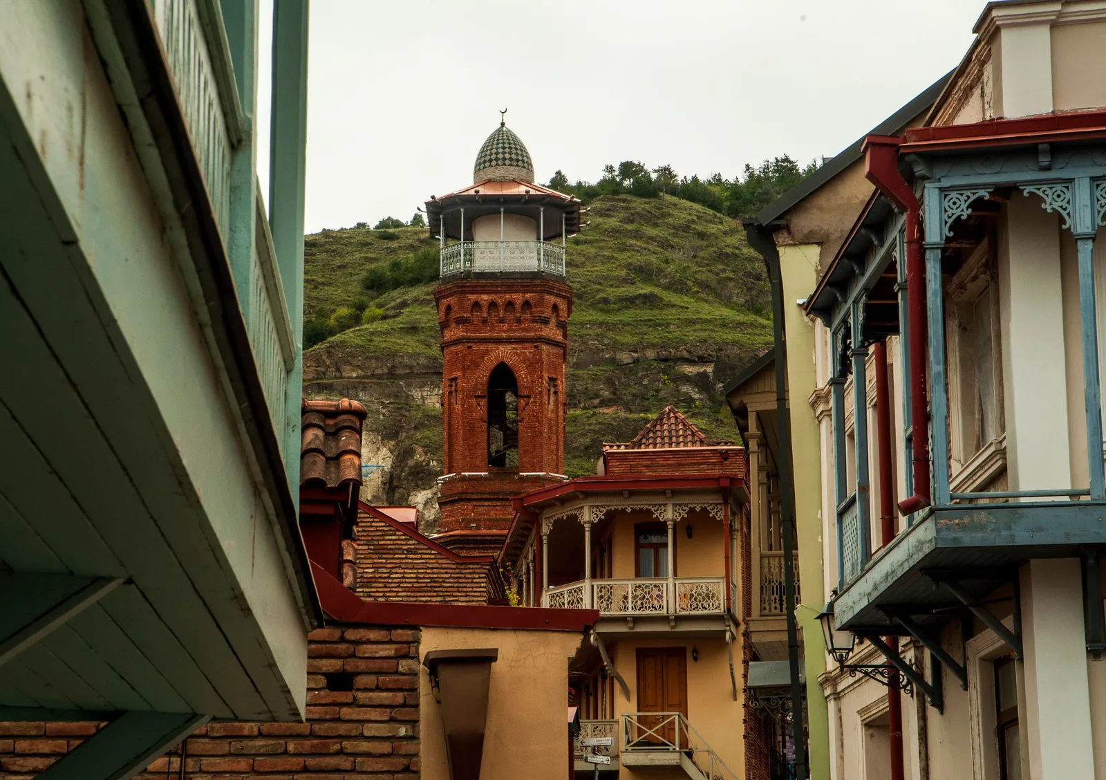 A cobbled old town street with balconied houses and a church tower in the Caucasus