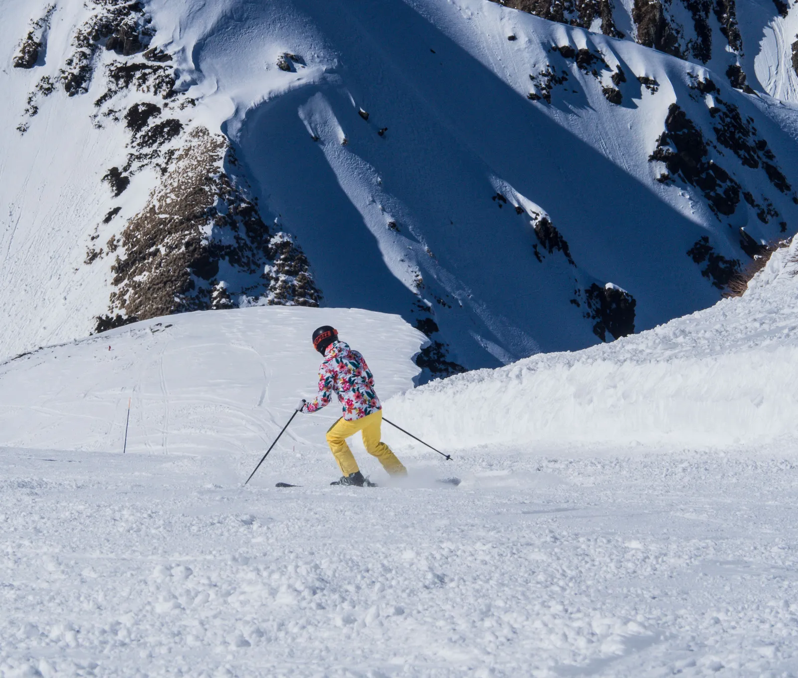 A skier turning on an open snow slope in the Georgian Caucasus with a steep face behind