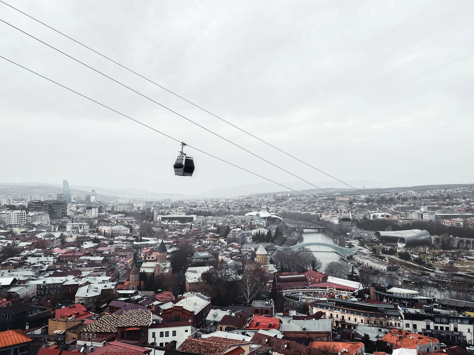 A cable car cabin crossing high above the rooftops of Tbilisi towards the ridge