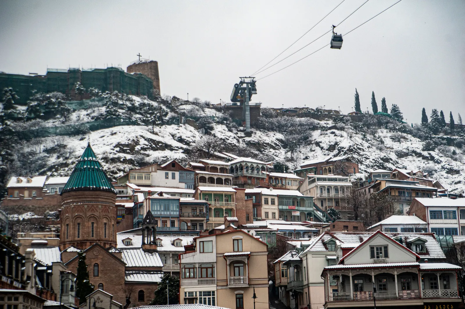 Snow on the roofs of old Tbilisi with the cable car line running up towards the fortress on the ridge