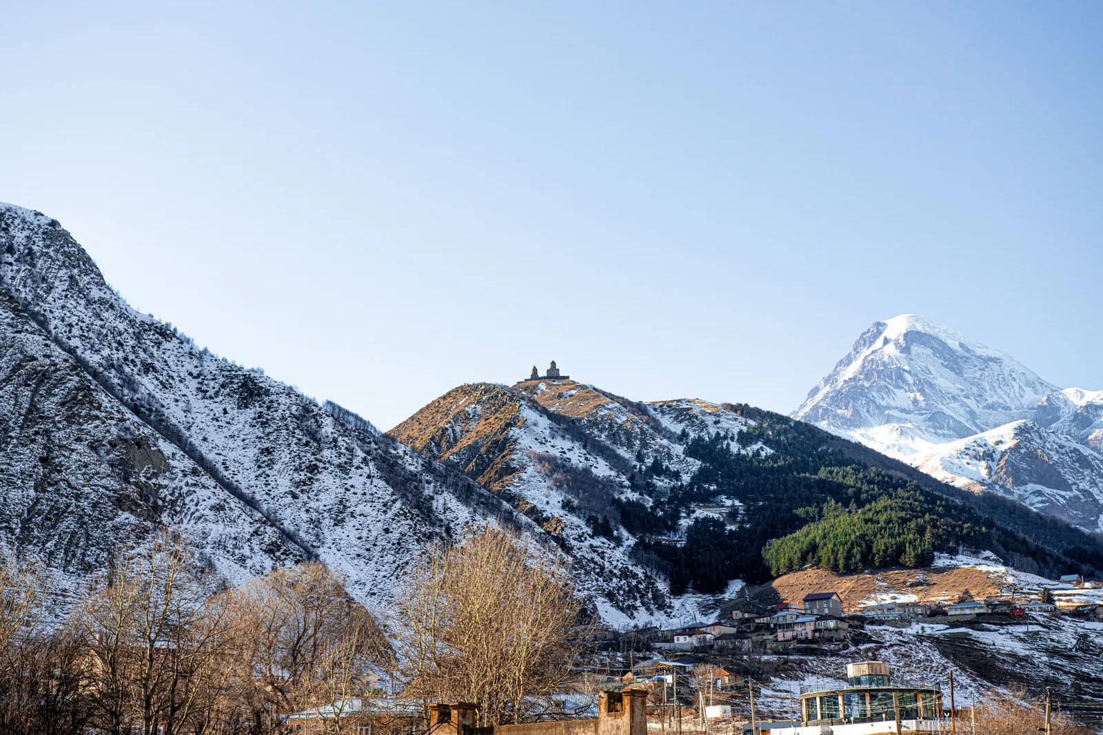 The village of Stepantsminda in its valley below the snow covered peak of Kazbek, with Gergeti Trinity small on the ridge to the left