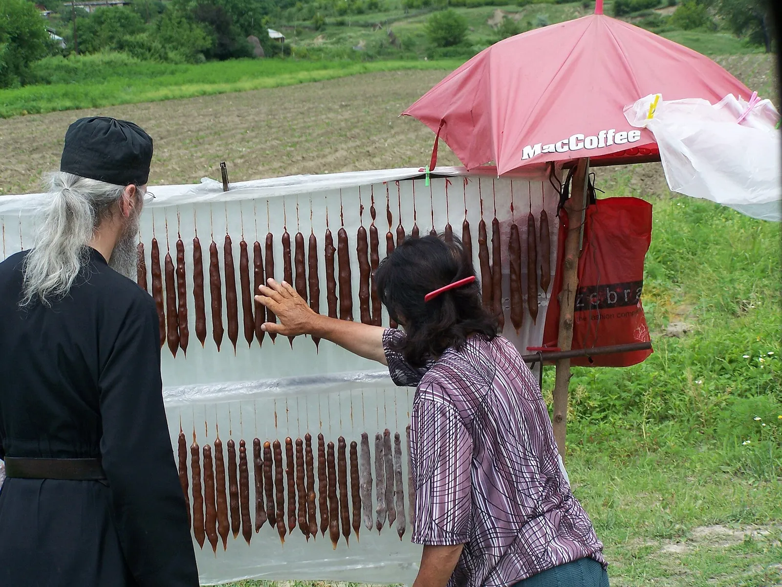 Rows of churchkhela hanging to dry at a roadside stall in Georgia, with fields behind
