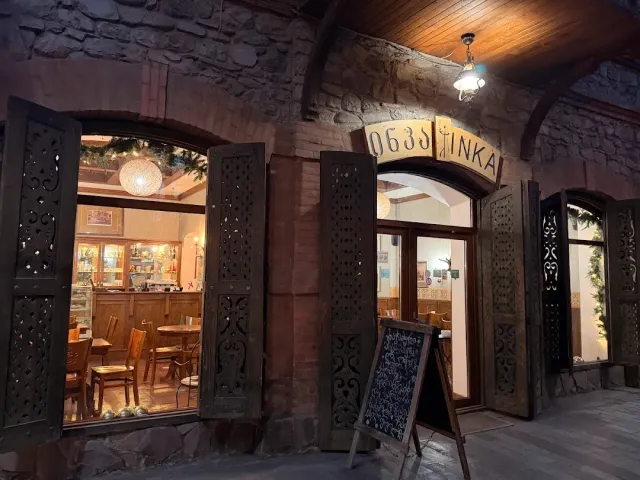 An arched stone facade in the evening with carved wooden shutters, a window into a lit room and a chalkboard