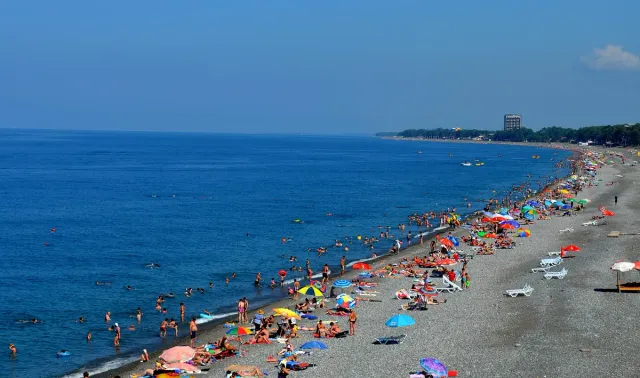 A long pebble beach lined with colourful umbrellas and bathers beside a blue sea