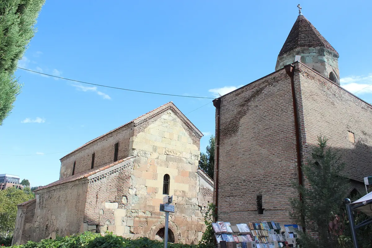 An ancient brick church with a conical bell tower, framed by trees under a blue sky