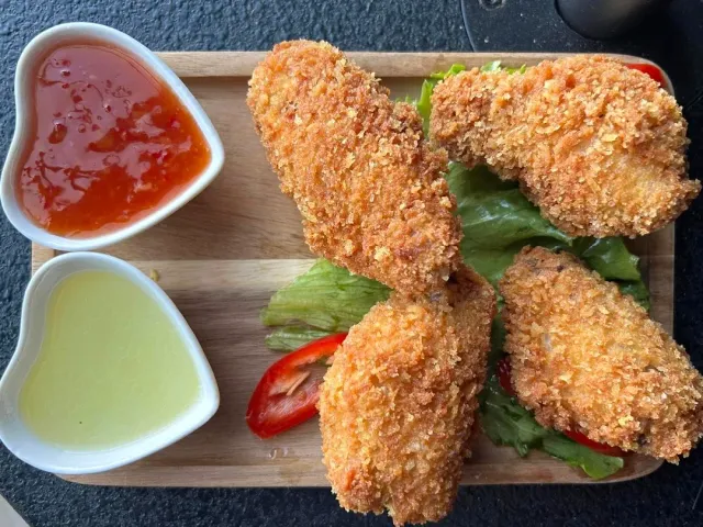 Crispy coated strips on a wooden board with lettuce and tomato and two sauces in white dishes