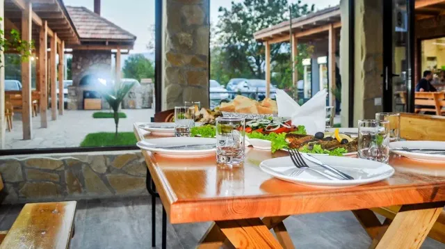 A wooden table set with plates and glasses on a covered veranda, and behind a stone wall and garden