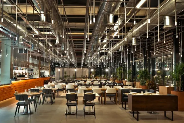 A huge industrial hall with exposed pipes, dozens of hanging lamps and rows of tables