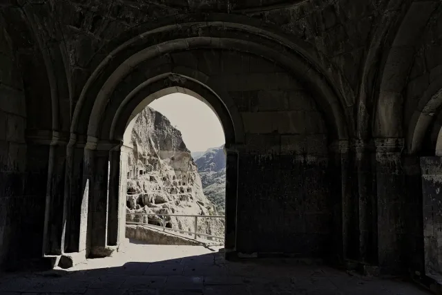 A vaulted stone hall opening onto a cliff face honeycombed with hundreds of carved caves