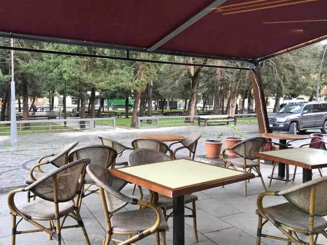 A covered terrace with wicker chairs and tables, with pine trees and a road behind it