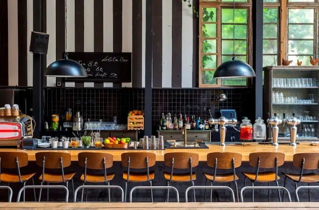 A long wooden counter with stools, black dome lamps and a white and black striped wall