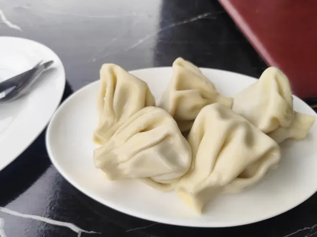 A plate with four hand folded dumplings on a dark marble table