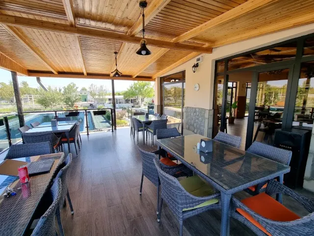 A covered terrace with a wooden ceiling, wicker armchairs, glass tables and a pool outside