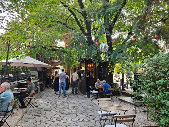 A stone-paved courtyard with small tables under trees and strings of red bulbs
