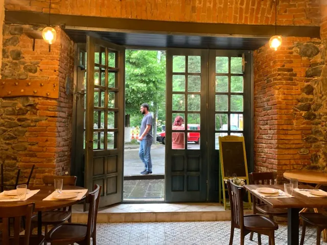 Green wooden doors open onto a shaded street, stone and brick walls and set tables