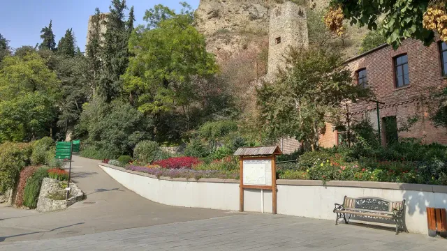 A paved path with flower beds and a bench, with a stone wall on the cliff above