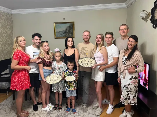 A group of people posing in a living room holding trays of dumplings they made
