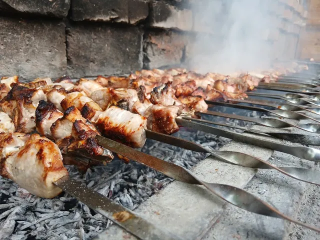 Meat skewers grilling over glowing embers in a smoky brick grill