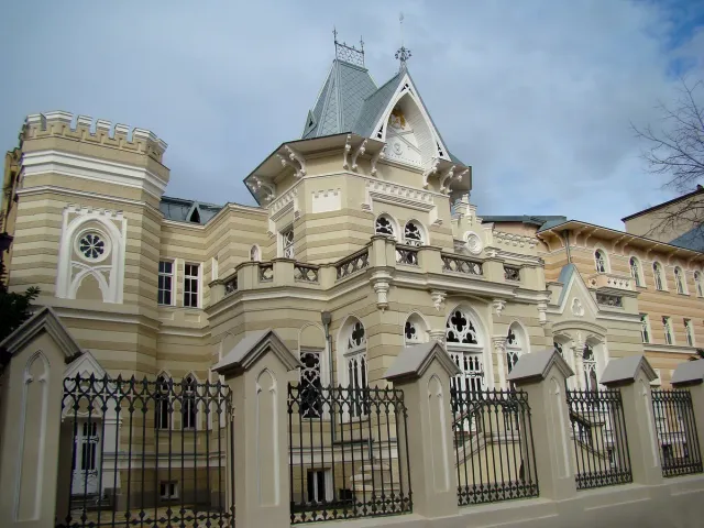An ornate turreted building with a clock and arched balconies behind an iron fence
