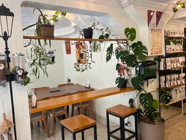 A seating corner with a wooden table, tall stools, plants and shelves of coffee bean bags