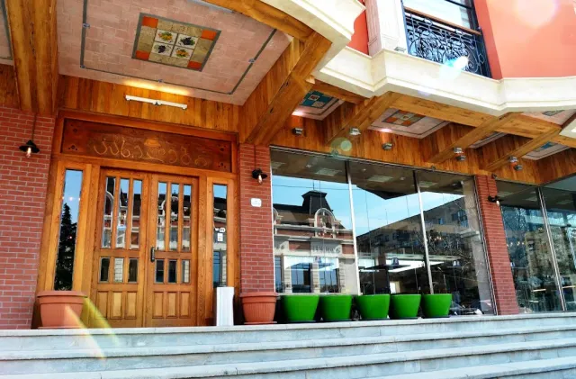 A building entrance with carved wooden doors, a wooden canopy, green pots and a glass front