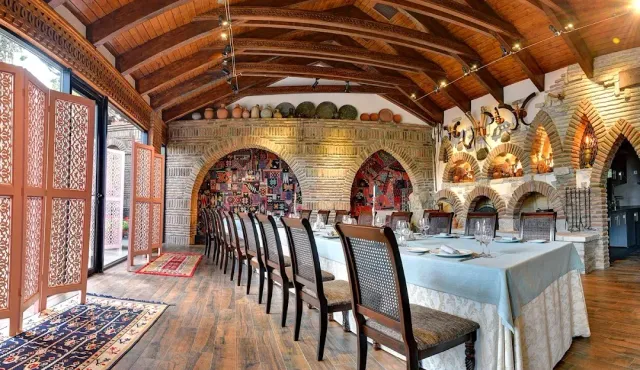A hall with a vaulted wooden ceiling, stone arches, clay jugs and a long set table