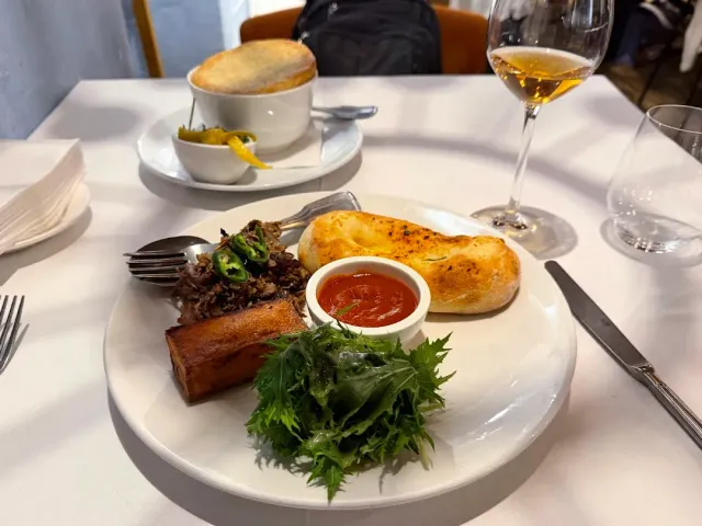 A plate with a marrow bone, chopped meat, baked bread and red sauce beside a glass of wine