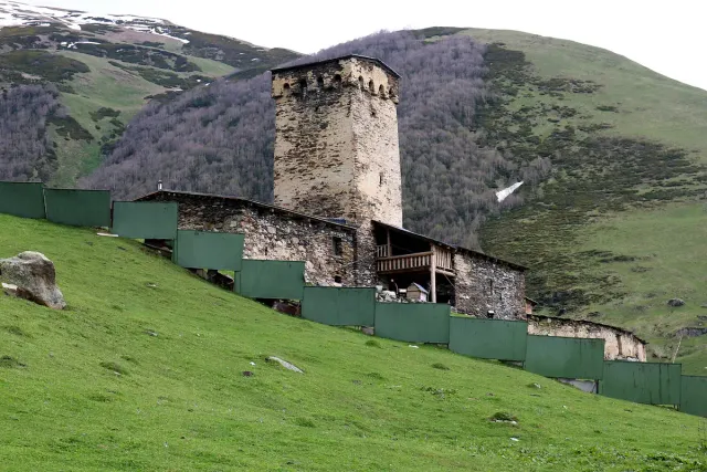 A stone Svan tower and a small church inside a wall on a green slope