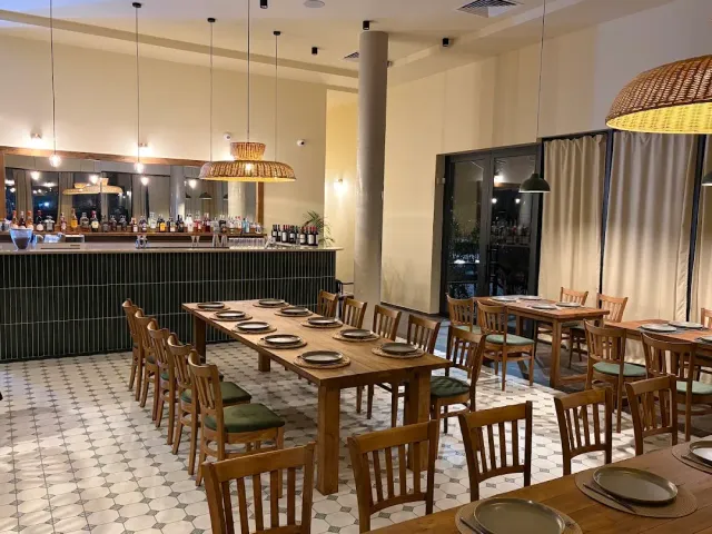 Long wooden tables with hanging wicker lamps, a green counter and a patterned tile floor