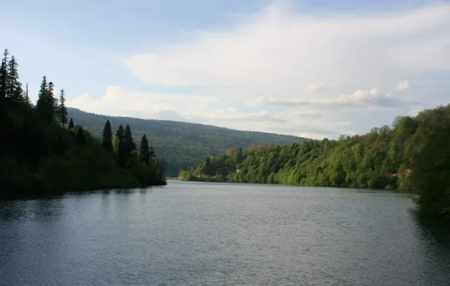 A calm lake ringed by wooded hills under a cloudy sky
