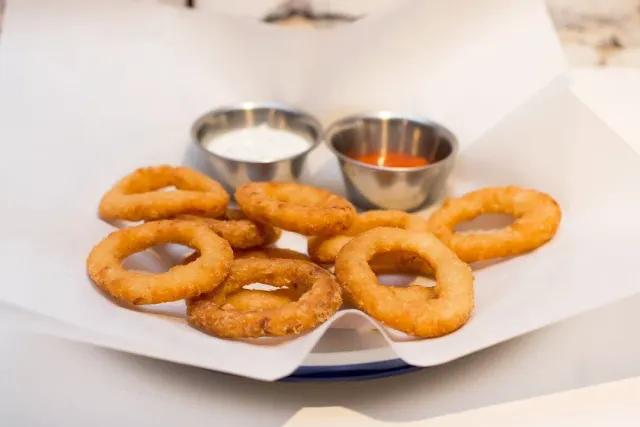 Fried onion rings on white paper beside two sauces in small pots