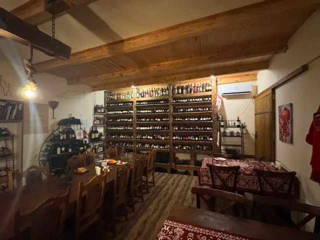 A room with wooden beams, shelves packed with wine bottles, a long table and carpets