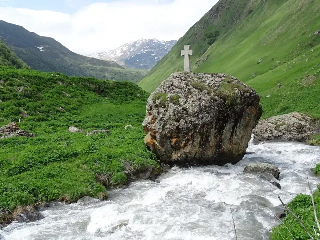 A giant boulder carved with a cross in a stream bed between green slopes