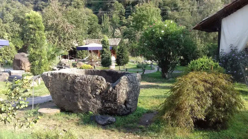 A traditional stone winepress on the lawn at Adjarian Wine House, with the winery building and wooded hills behind