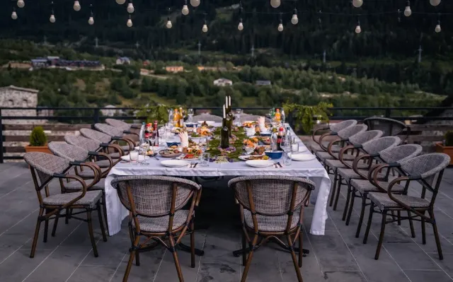 A long table in a white cloth on a terrace, cane chairs, hanging bulbs and a green valley