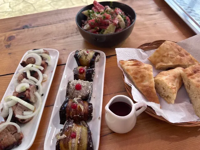 A wooden table with eggplant rolls, grilled meat with onion, a vegetable salad and baked bread