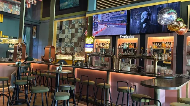 A bar counter lit in pink with stools, beer taps, bottle shelves and screens on the wall