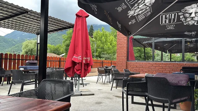 A covered seating terrace with dark chairs and parasols, facing forested mountains and clouds