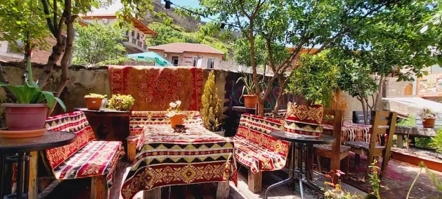 Benches upholstered with colourful rugs in a courtyard, a stone wall, trees and houses on a slope