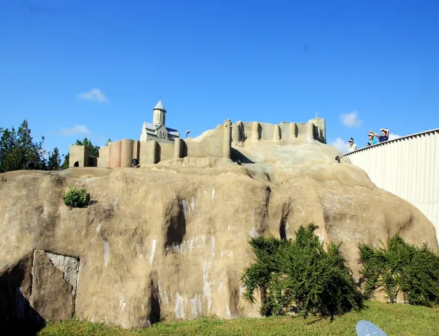 A scale model of a fortress and a church on an artificial rock, with visitors in the background