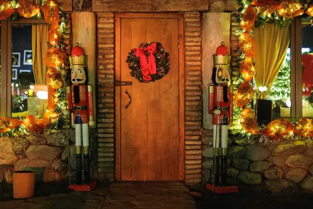 A wooden door decorated with a festive wreath between two wooden soldier figures and strings of lights