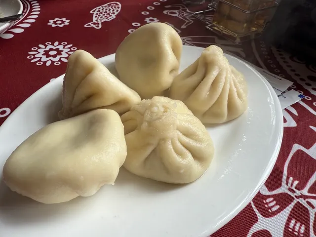 A plate of steaming khinkali on a red tablecloth with a white pattern