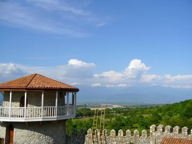 A tiled roof wooden pavilion with a white balustrade on a stone wall, facing a wide valley and mountains
