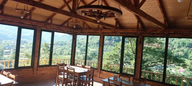 A glazed pavilion with a wooden ceiling and a wheel chandelier, plain tables and a view of green hills